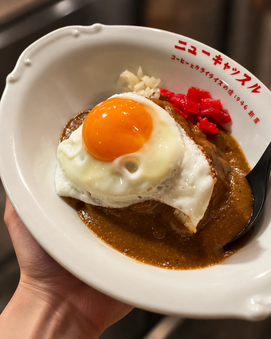 手に持った皿の、目玉焼きをのせたカライライスの寄り